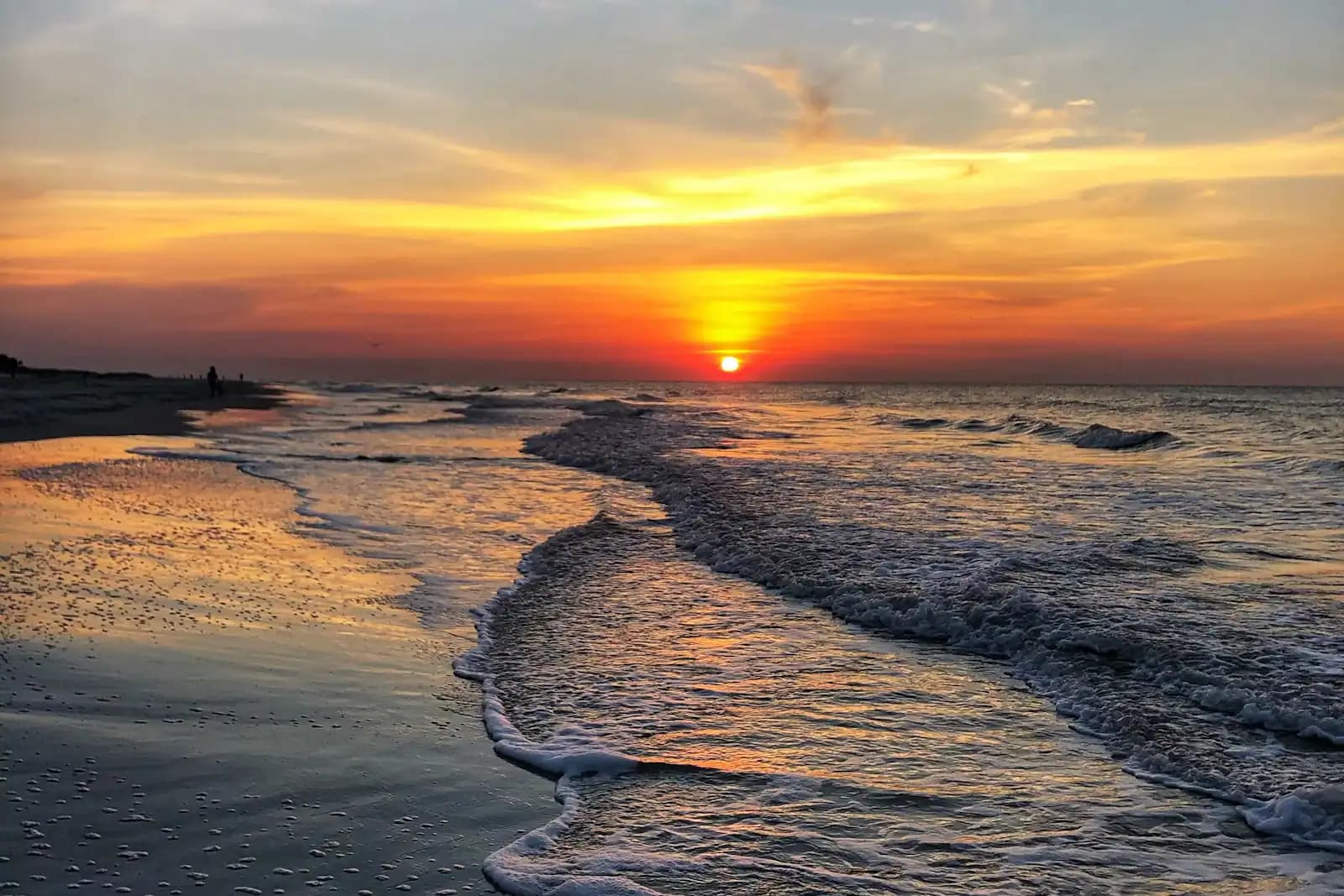 Low waves breaking along a wide, flat stretch of beach in late evening light